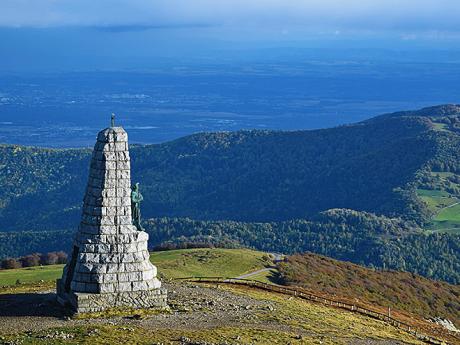 Mohyla shlížející na zalesněné zaoblené vršky pohoří Vogézy